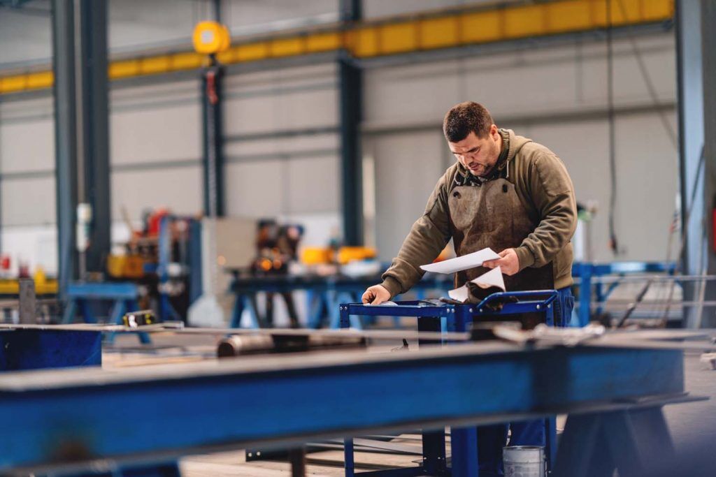 Industrial worker is looking at blueprint in a large factory hall.