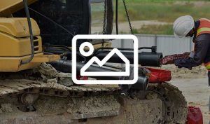 A construction worker is inspecting or cleaning a large excavator or tracked vehicle at a job site.